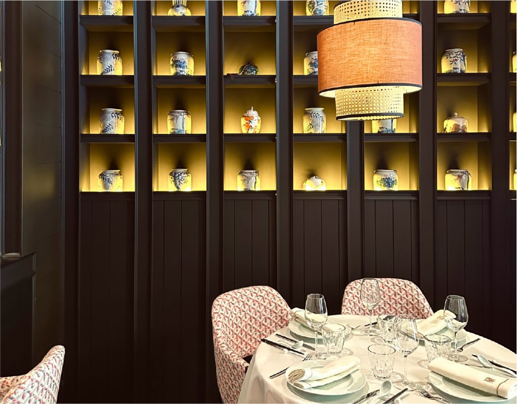 Elegante comedor de Mandarin Palace con mesa redonda vestida de blanco, sillas estampadas y estanterías iluminadas con jarrones decorativos asiáticos.