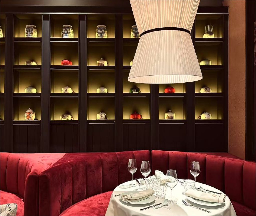Elegante salón privado en Mandarin Palace Barcelona con sofá aterciopelado rojo, mesa redonda vestida de blanco y estanterías iluminadas con jarrones decorativos asiáticos.